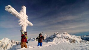 Paisaje nevado de montañas con una persona de pie en la cima cubierta de nieve.