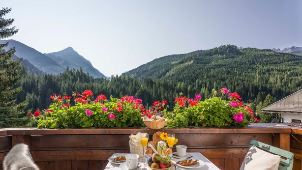 A table set with breakfast items, a wooden bench, and a view of a forested mountain range.