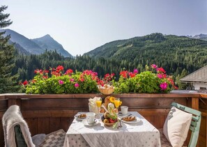 Une table dressée avec des aliments pour le petit-déjeuner, un banc en bois et une vue sur les montagnes et la forêt.