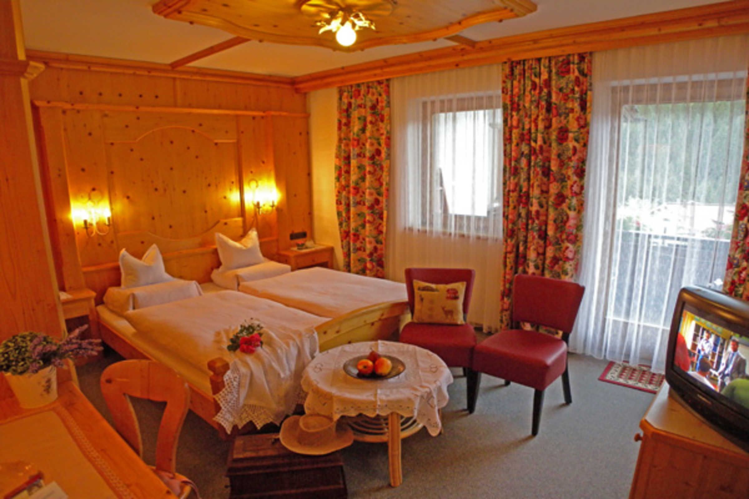 A hotel room with two beds, a TV, a red chair, and a small table with a fruit bowl.