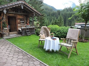 A rustic wooden cabin with a porch, a table with chairs, and a garden. - Apartment 3 - Landhaus Dengg (Gerlos)