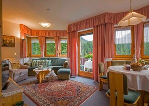 A cozy room with a sofa, chairs, a dining table, and a large window with curtains. - Apartment 3 - Landhaus Dengg (Gerlos)