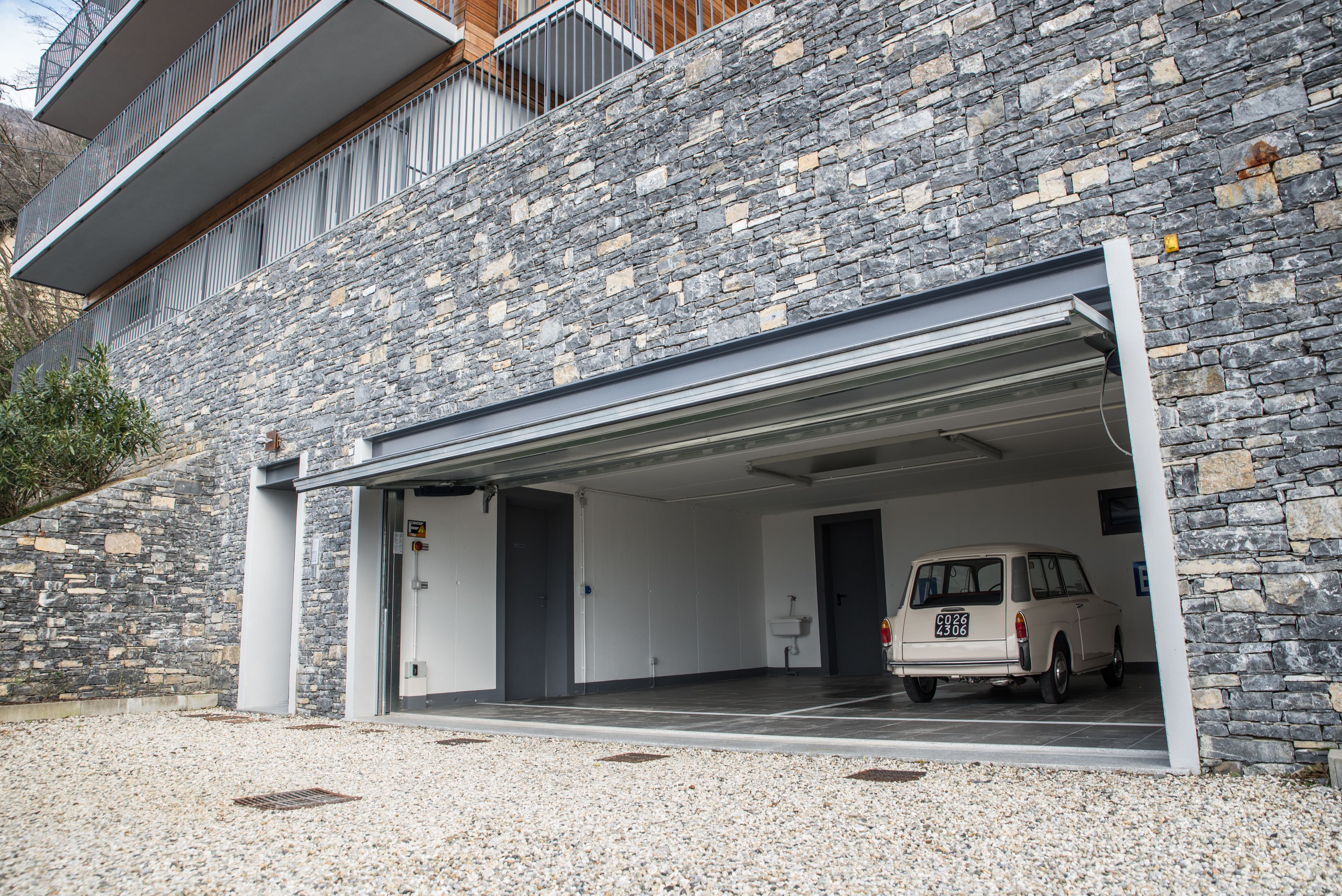 A modern building with a stone facade, a covered parking area, and a parked van.