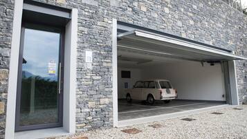 A modern building with a stone facade, a garage with a white car inside, and a gravel driveway.