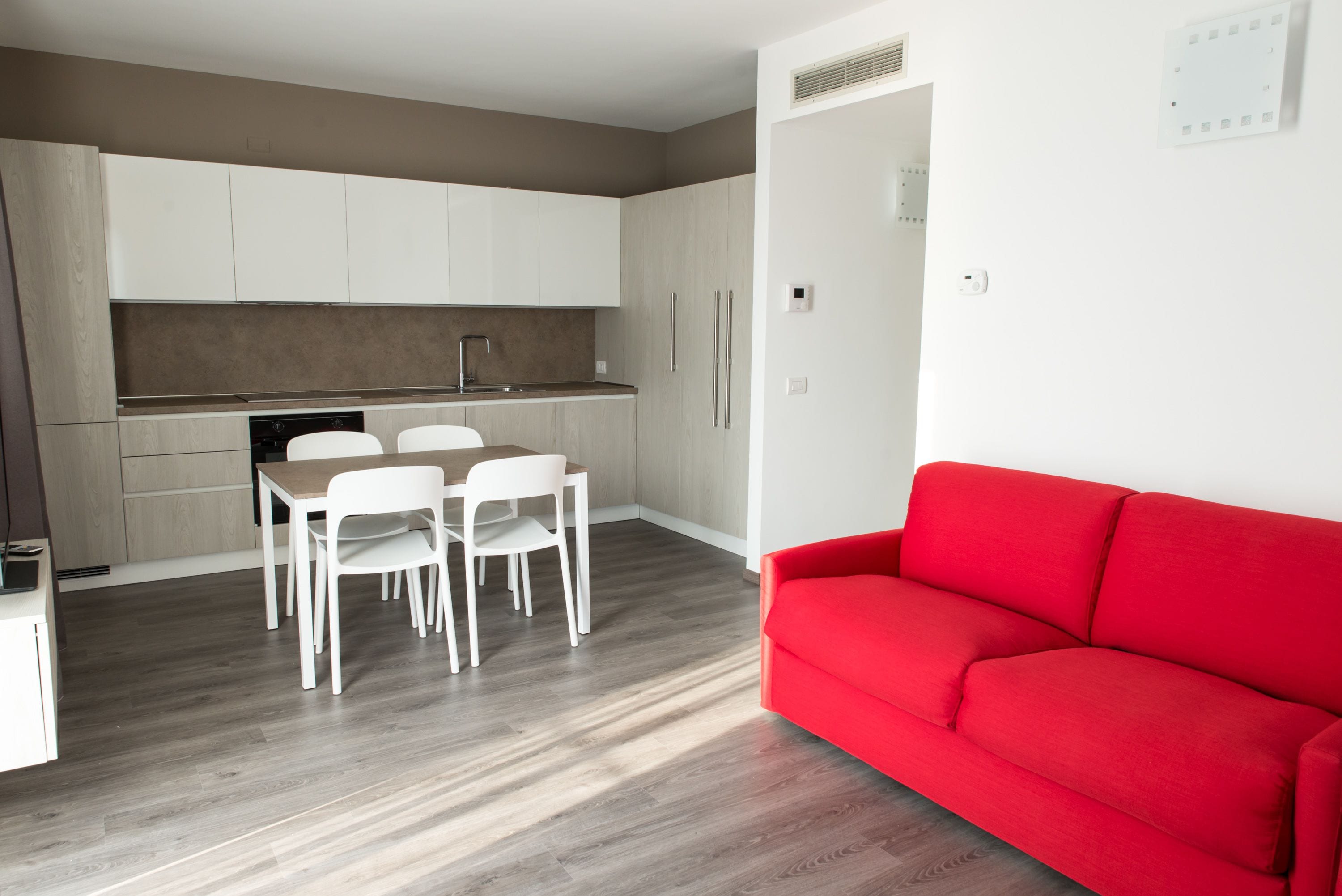 A modern kitchen with white cabinets, a dining table with chairs, and a red sofa.