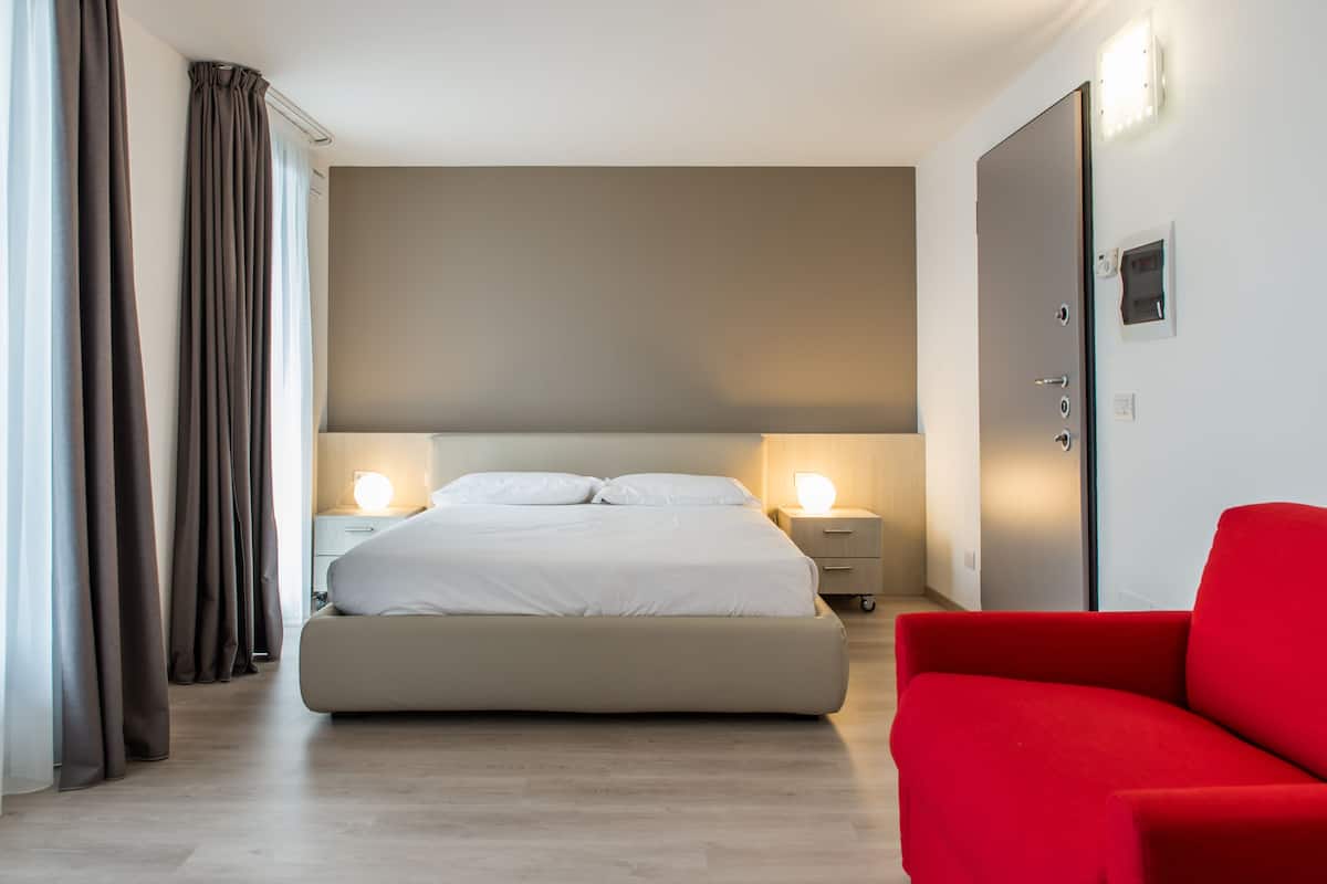 A modern hotel room with a large bed, bedside lamps, a red chair, and a wardrobe.