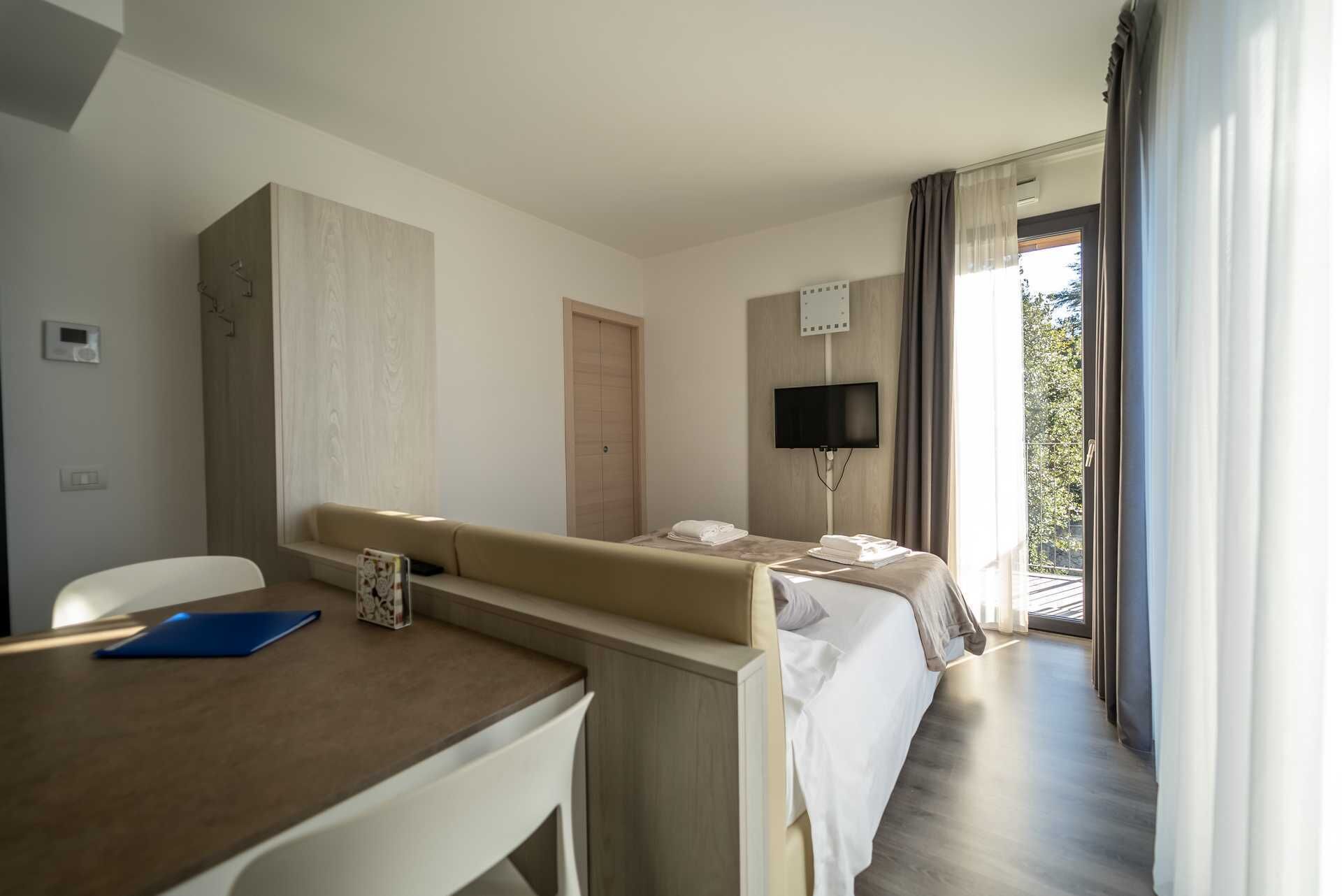 Una habitación de hotel con cama, escritorio, silla, televisión y ventana con cortinas.