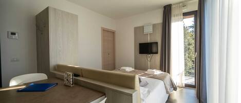 Una habitación de hotel con cama, escritorio, silla, televisión y ventana con cortinas.