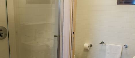 A glass-enclosed shower with a white towel hanging on the door, a toilet with a roll of toilet paper, and a towel rack with two towels.