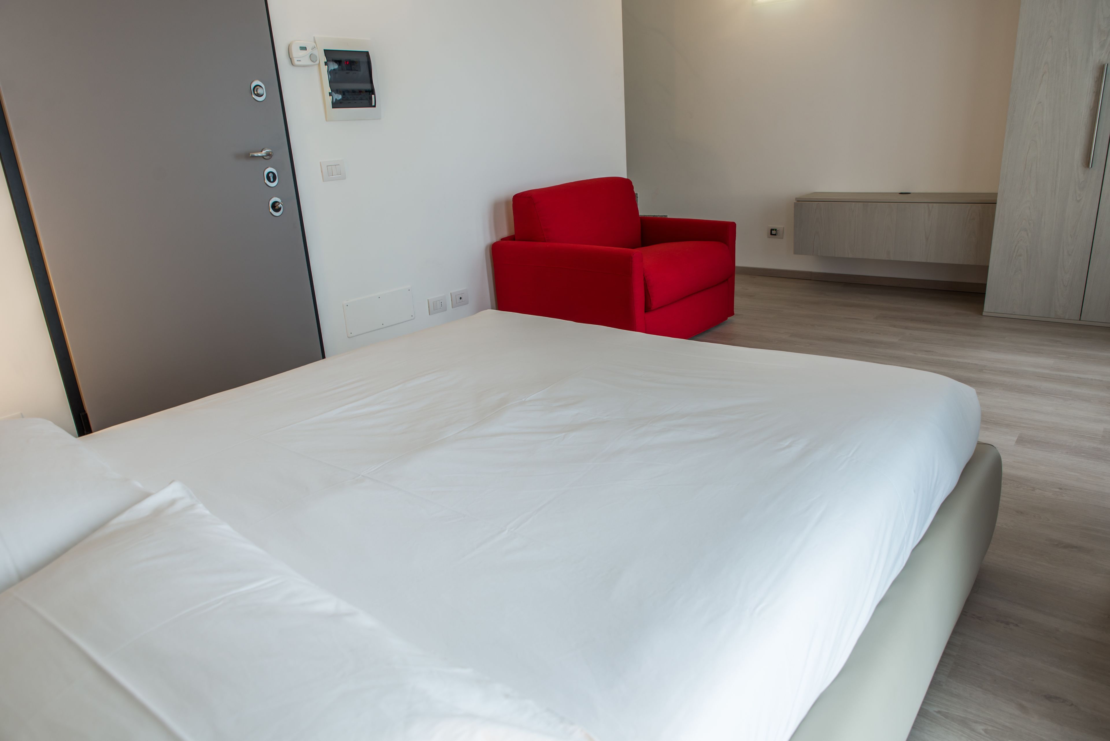 Een moderne hotelkamer met een groot bed, een rode fauteuil en een inbouw kast.