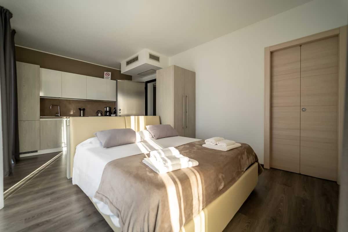 A hotel room with a bed, a small kitchenette, a wardrobe, and a bathroom.