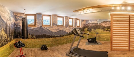 Une salle de sport à domicile équipée d’un tapis de course, d’un vélo d’appartement, d’un sac de frappe et d’autres appareils d’exercice.