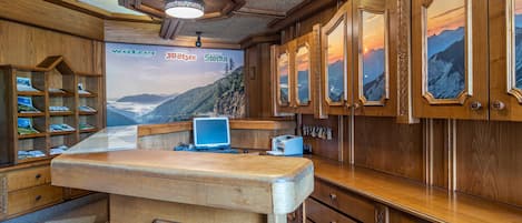 Un mostrador de recepción de madera con una computadora, una estantería con revistas y una pared con cuadros enmarcados.