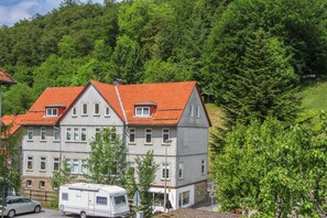 A two-story building with a red-tiled roof, multiple windows, and a parked camper in front.