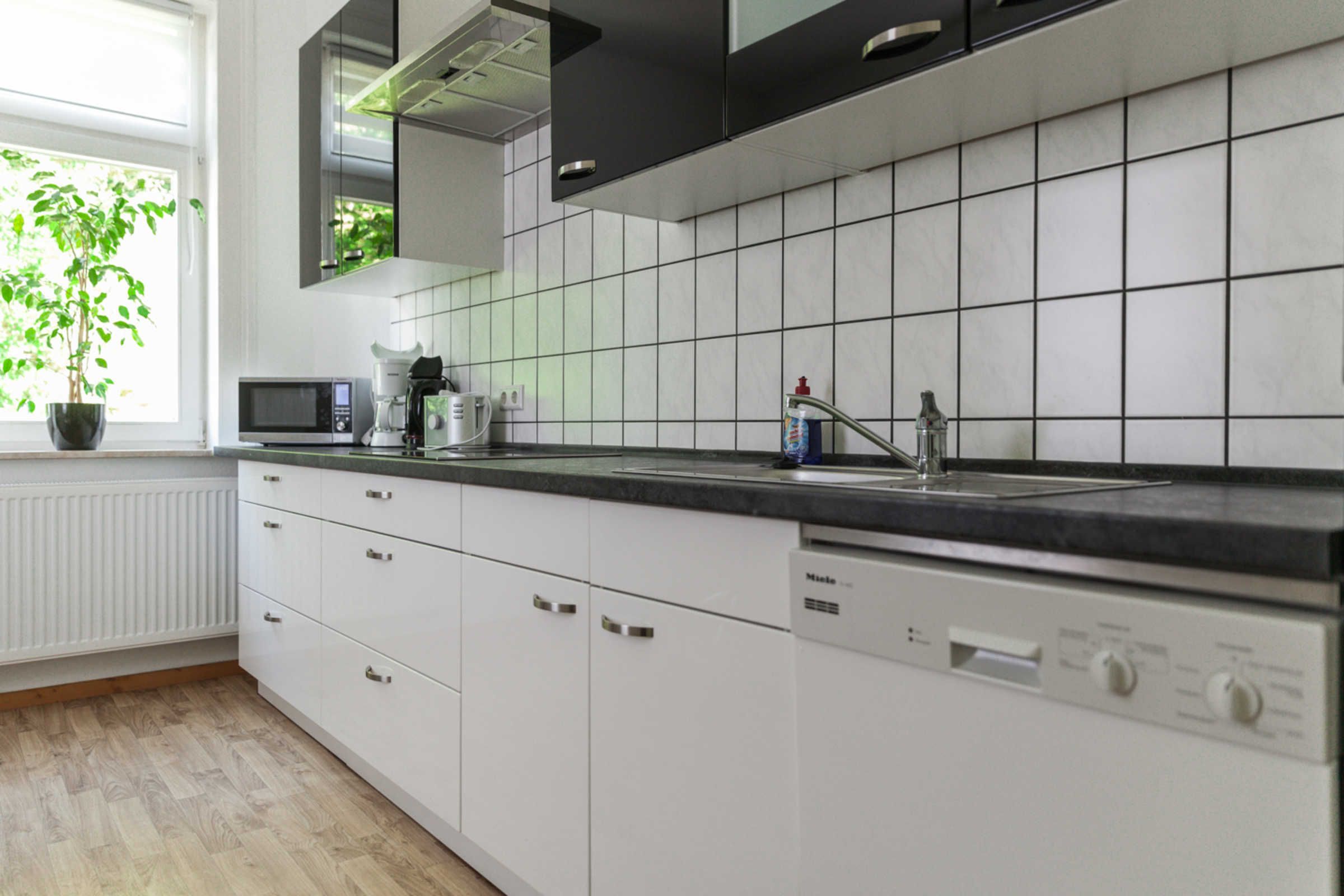 A modern kitchen with white cabinets, a black countertop, a microwave, a coffee maker, and a dishwasher.