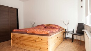 En seng i træ med et mønstret tæppe, et lille natbord med en lampe, en stol og et klædeskab.
