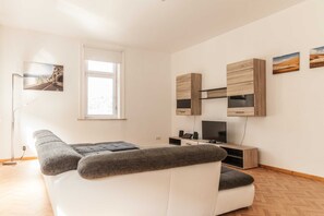 A modern living room with a sofa, a flat-screen TV, wooden cabinets, and artwork on the walls.