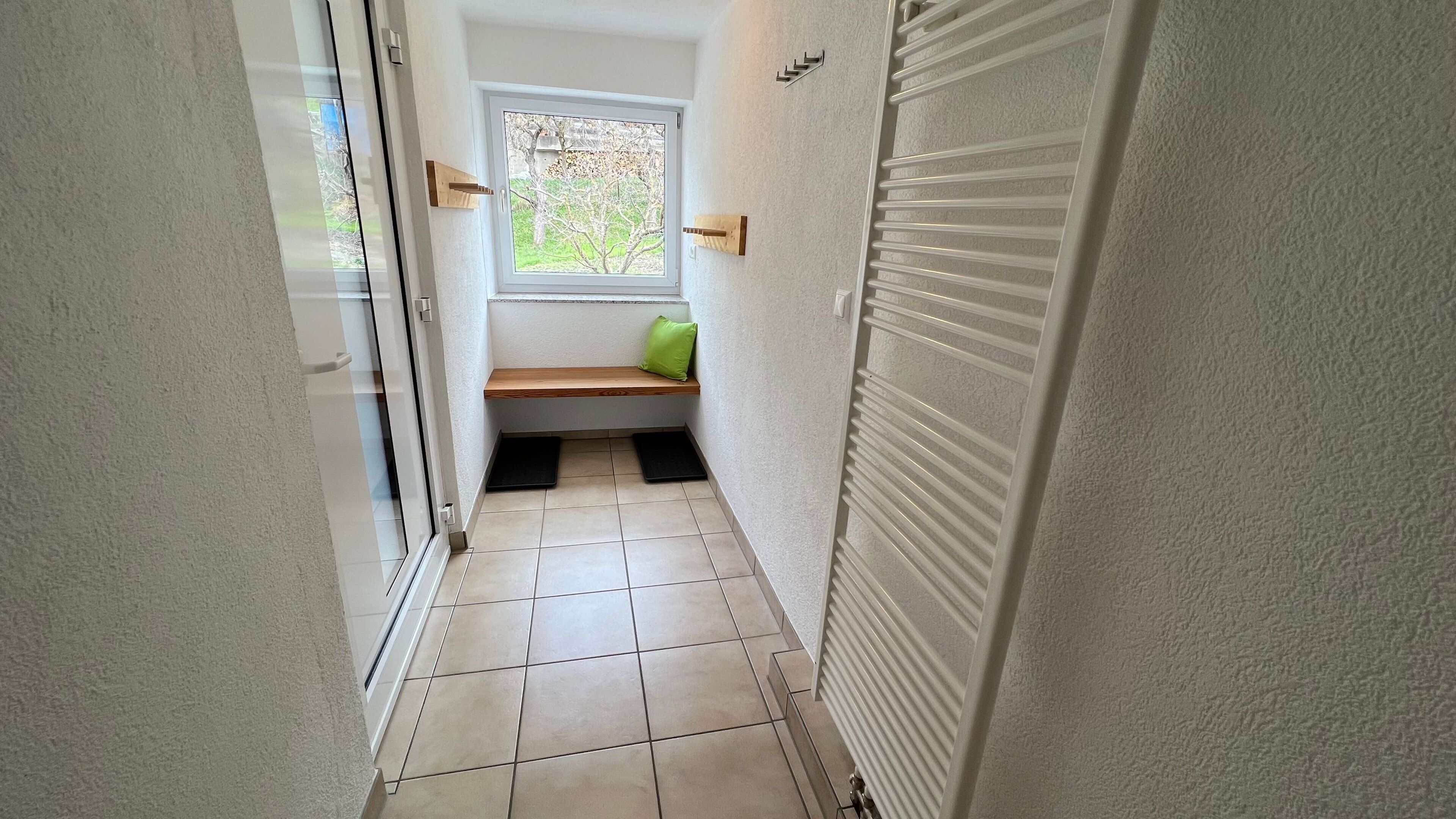 Ein schmaler Flur mit einer Bank, einem Fenster und einer Schiebetür.