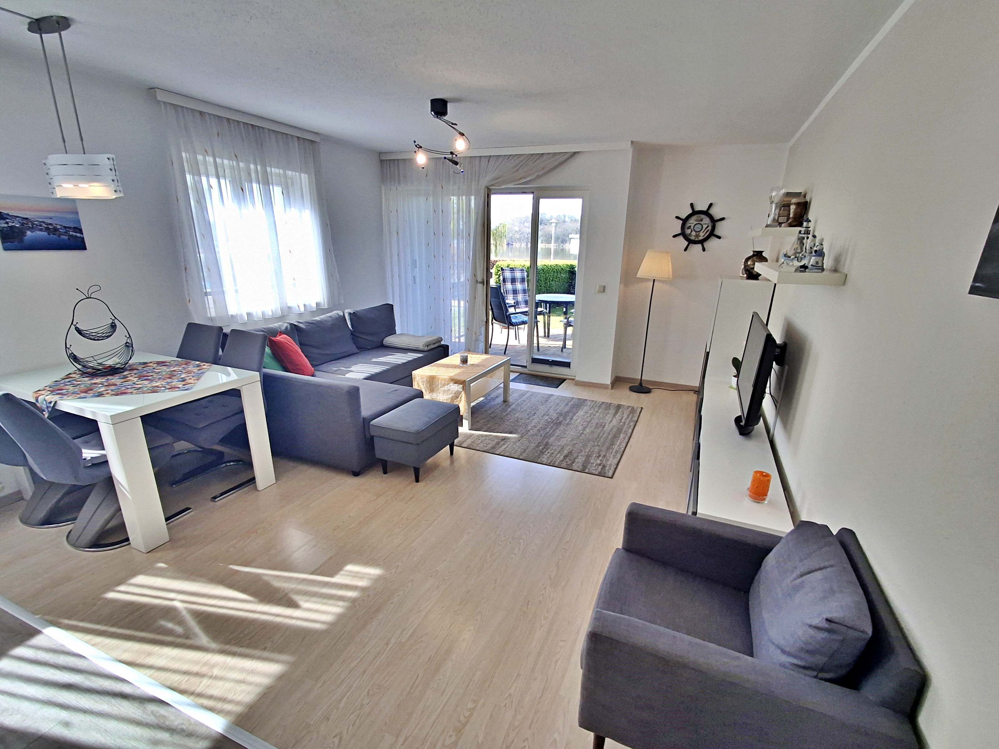 Un salon moderne avec un canapé, une table à manger et une table basse. On y trouve une grande fenêtre avec des rideaux, un luminaire au plafond et une horloge murale.