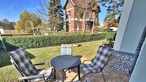 Een buitenpatio met een ronde tafel en vier geruite stoelen.