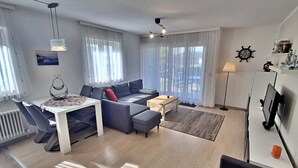 Een moderne woonkamer met een eetgedeelte, grijze banken, een salontafel en een tv op een meubel.