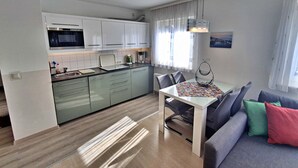 Een moderne keuken met witte kasten, een eettafel met stoelen, en een bank met kussens.