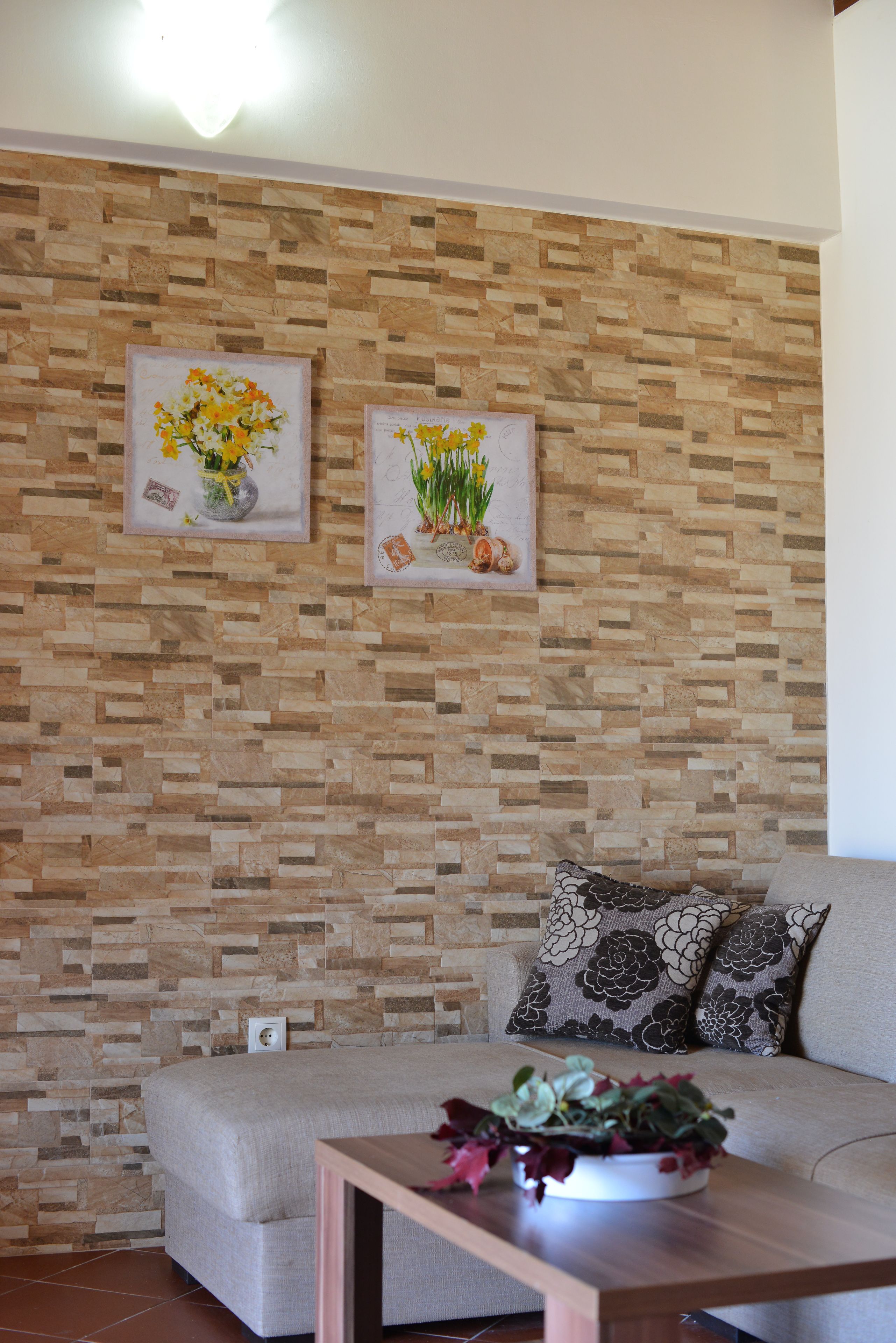 Un salon avec un mur orné d’un motif, un canapé, deux coussins et une table d’appoint sur laquelle est posée une plante.