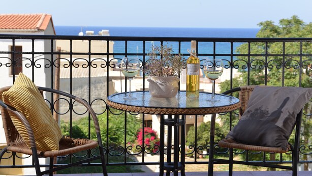 A balcony with wicker chairs, a small round table, and a view of the sea. - Castello Domus (Mylopotamos)
