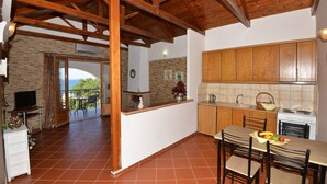 A compact kitchen with wooden cabinets, a dining table with chairs, a TV, and a balcony with a view. - Castello Domus (Mylopotamos)