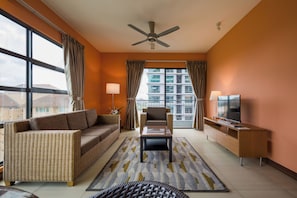A living room with a sofa, armchair, coffee table, TV stand, and a ceiling fan. - Acappella Suite Hotel (Shah Alam)