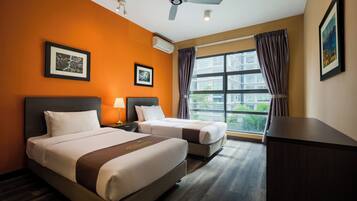 Una habitación de hotel con dos camas, ventilador de techo, ventanas amplias con cortinas y cuadros en las paredes.
