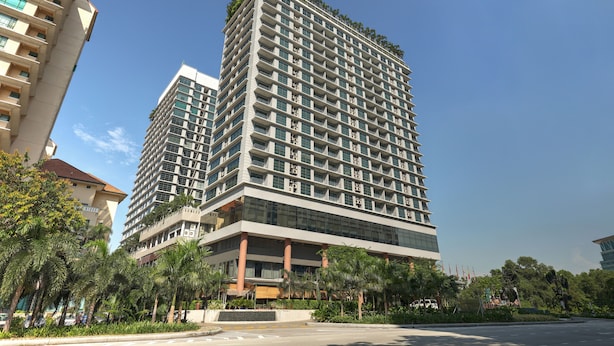 Un hotel moderno de gran altura con numerosos pisos, amplias ventanas y una terraza verde en la azotea.