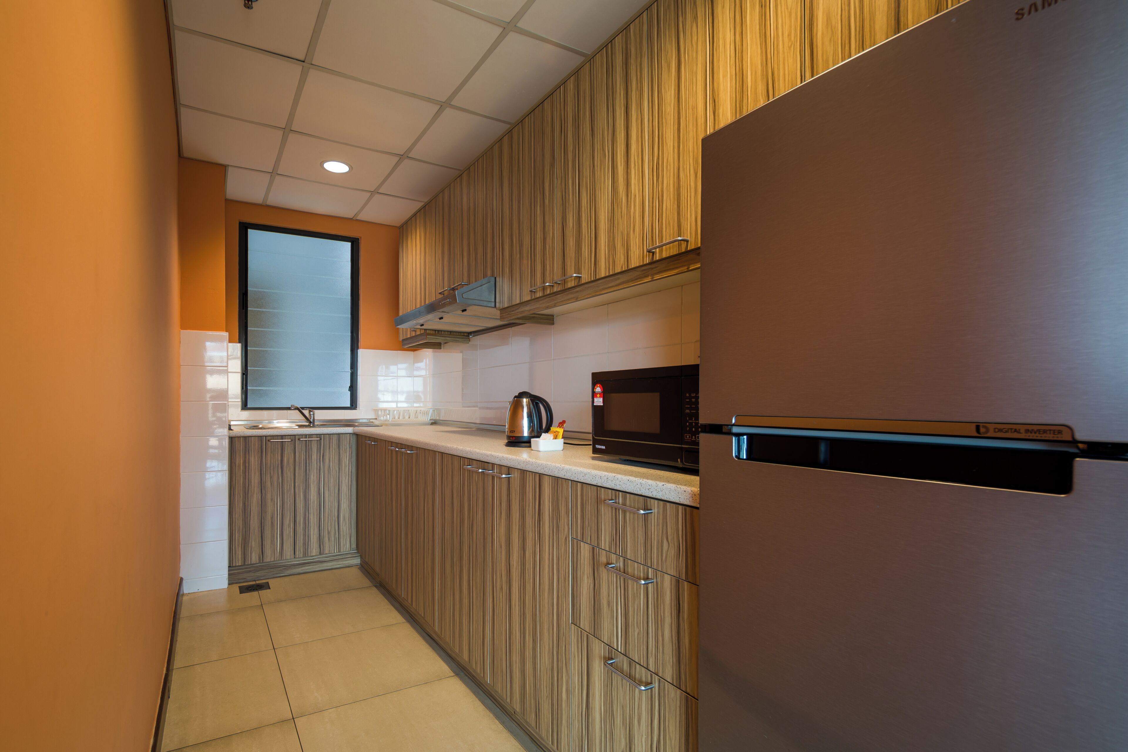 Eine moderne Küche mit Holzschränken, einem Edelstahlkühlschrank, einer Mikrowelle und einem Wasserkocher.