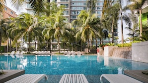 Una piscina con sillas de descanso, palmeras y un edificio moderno al fondo.