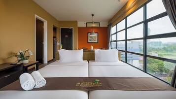 A hotel room with two beds, a large window, a wall-mounted air conditioner, and a view of greenery outside.