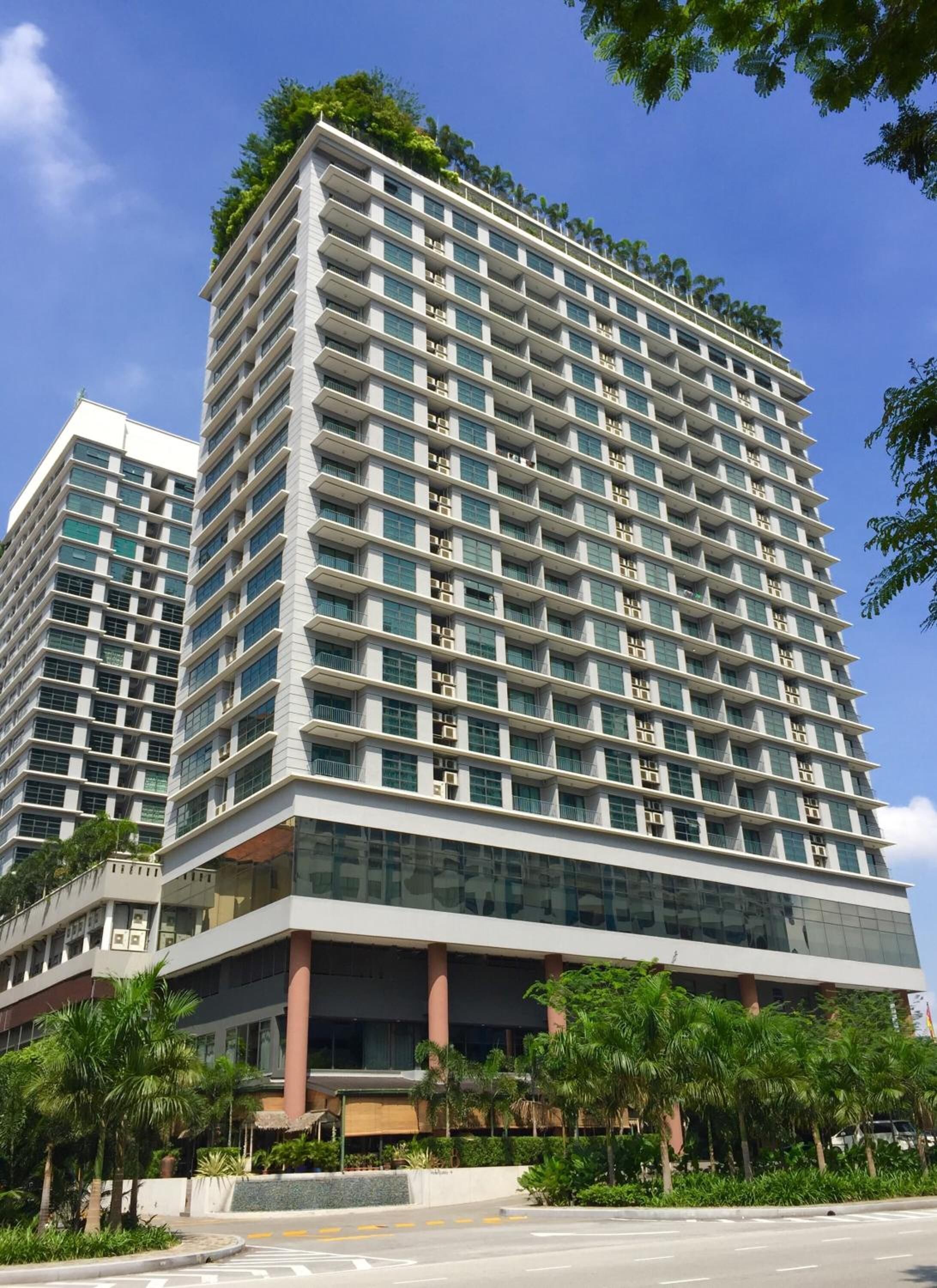 Un immeuble moderne de grande hauteur, doté de nombreux balcons, de grandes fenêtres et d’un toit plat agrémenté de verdure.