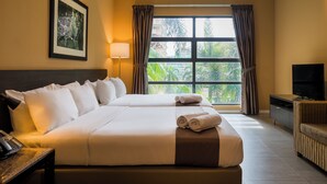 Habitación de hotel con dos camas, televisión, lámpara, un cuadro enmarcado y vista a zonas verdes.