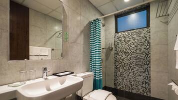 A bathroom with a large mirror, a sink, a toilet, a shower with a striped curtain, and a tiled wall.