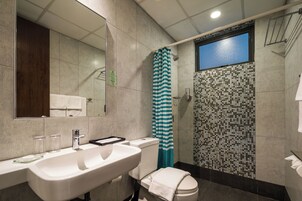 A bathroom with a large mirror, a sink, a toilet, a shower with a striped curtain, and a tiled wall.