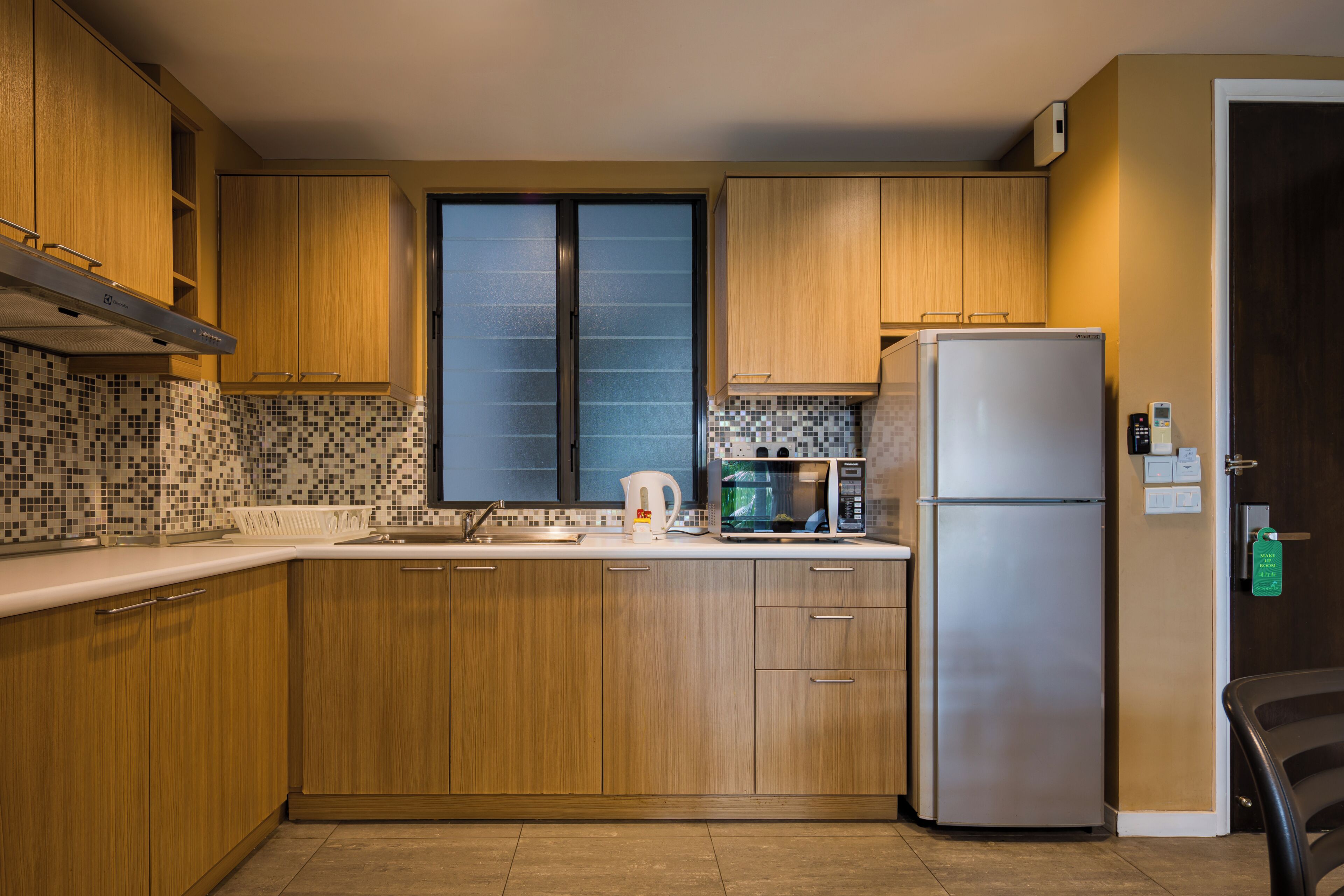 A kitchen with wooden cabinets, a stainless steel refrigerator, a microwave, and a window with frosted glass.