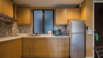 A kitchen with wooden cabinets, a stainless steel refrigerator, a microwave, and a window with frosted glass.