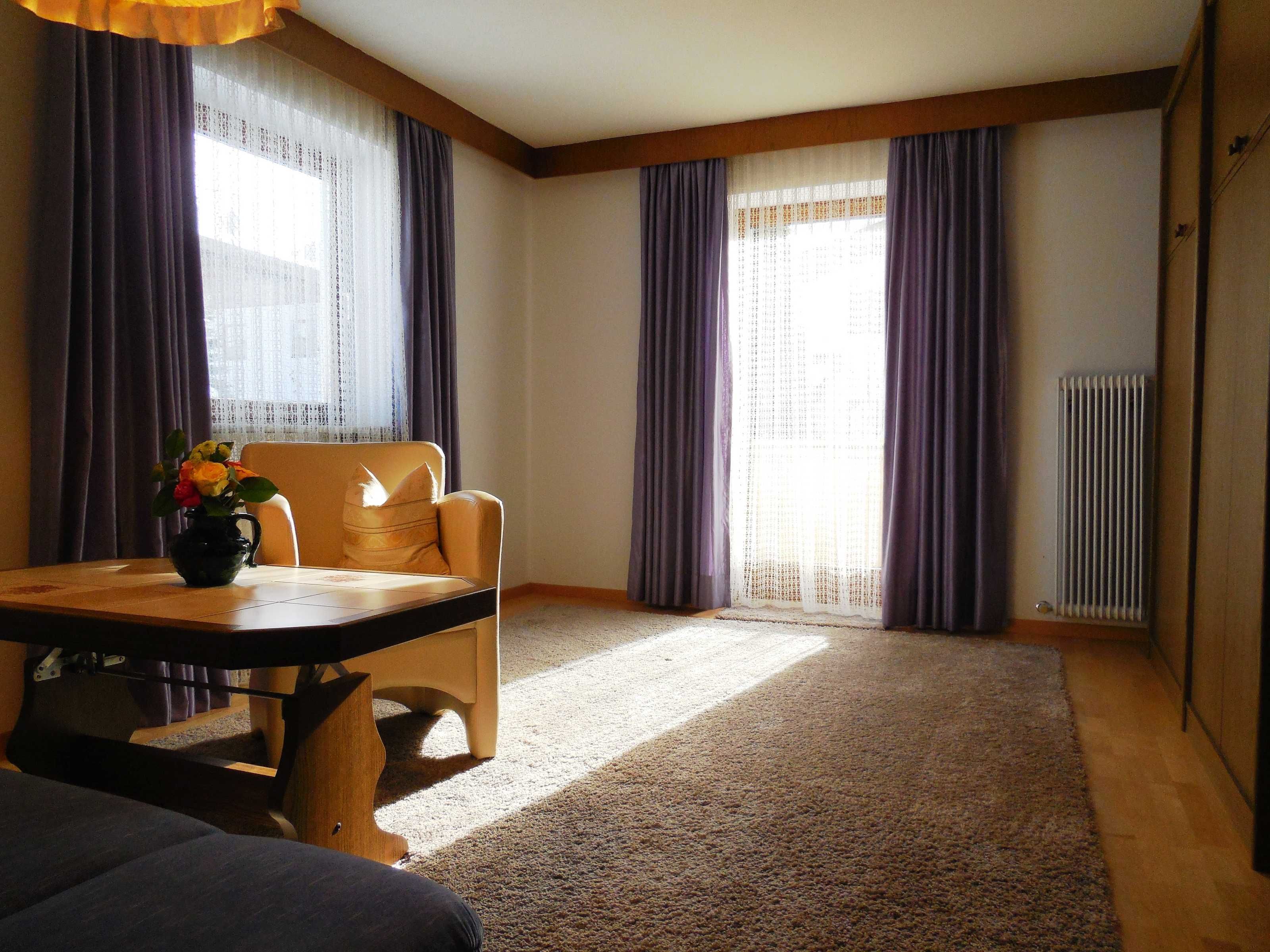 A room with a wooden table, a chair, a vase with flowers, and a radiator.