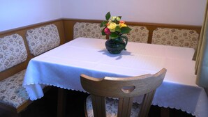 Un coin repas avec une table recouverte d’une nappe blanche, des chaises à motifs floraux et un vase rempli de fleurs.