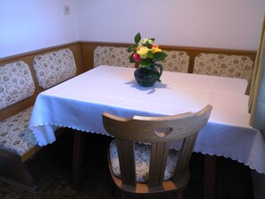 Un comedor con una mesa cubierta con mantel blanco, sillas estampadas con motivos florales y un florero con flores.