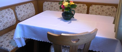A dining area with a table covered in a white tablecloth, floral-patterned chairs, and a vase with flowers.