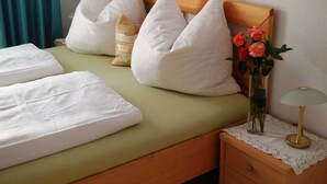 Un lit bien fait, avec du linge de lit blanc, une couvre-lit verte et des coussins décoratifs. On peut voir un vase rempli de fleurs sur la table de chevet, à côté du lit.
