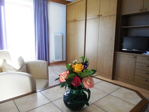 Una sala de estar con un sofá, una mesa con un florero, un radiador y un televisor sobre un mueble de madera.