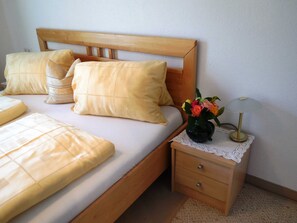 Una cama bien tendida con ropa de cama amarilla, un cabecero de madera y una mesita de noche con un jarrón de flores y una lámpara.