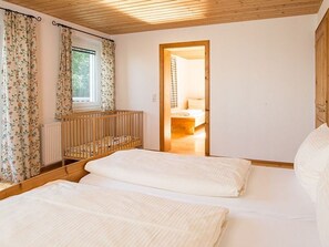 Ein Schlafzimmer mit zwei Betten, einer Holzbalkendecke, einem Fenster mit Vorhängen und einer Tür zu einem weiteren Zimmer.