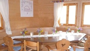 Interior de una cabaña de madera con una mesa redonda de comedor, seis sillas de madera y centros de mesa florales.